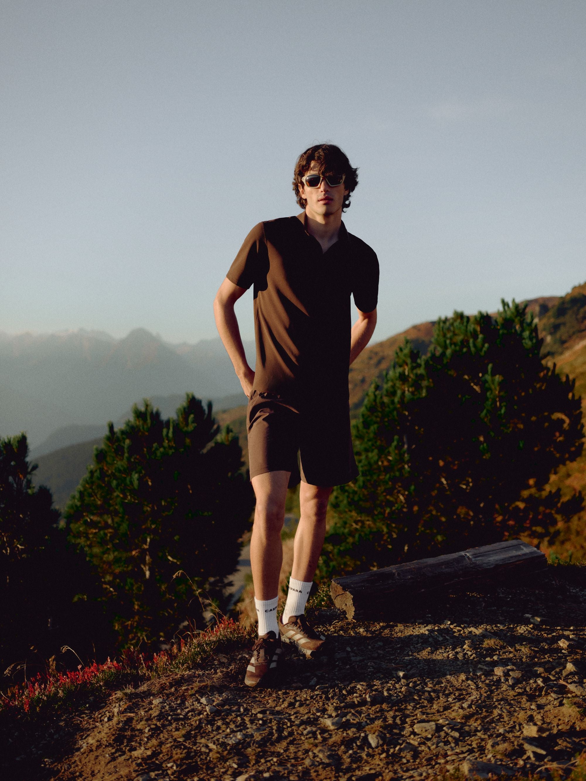 Man wearing an espresso CASPARA Vantage polo tee standing on a mountain hillside.
